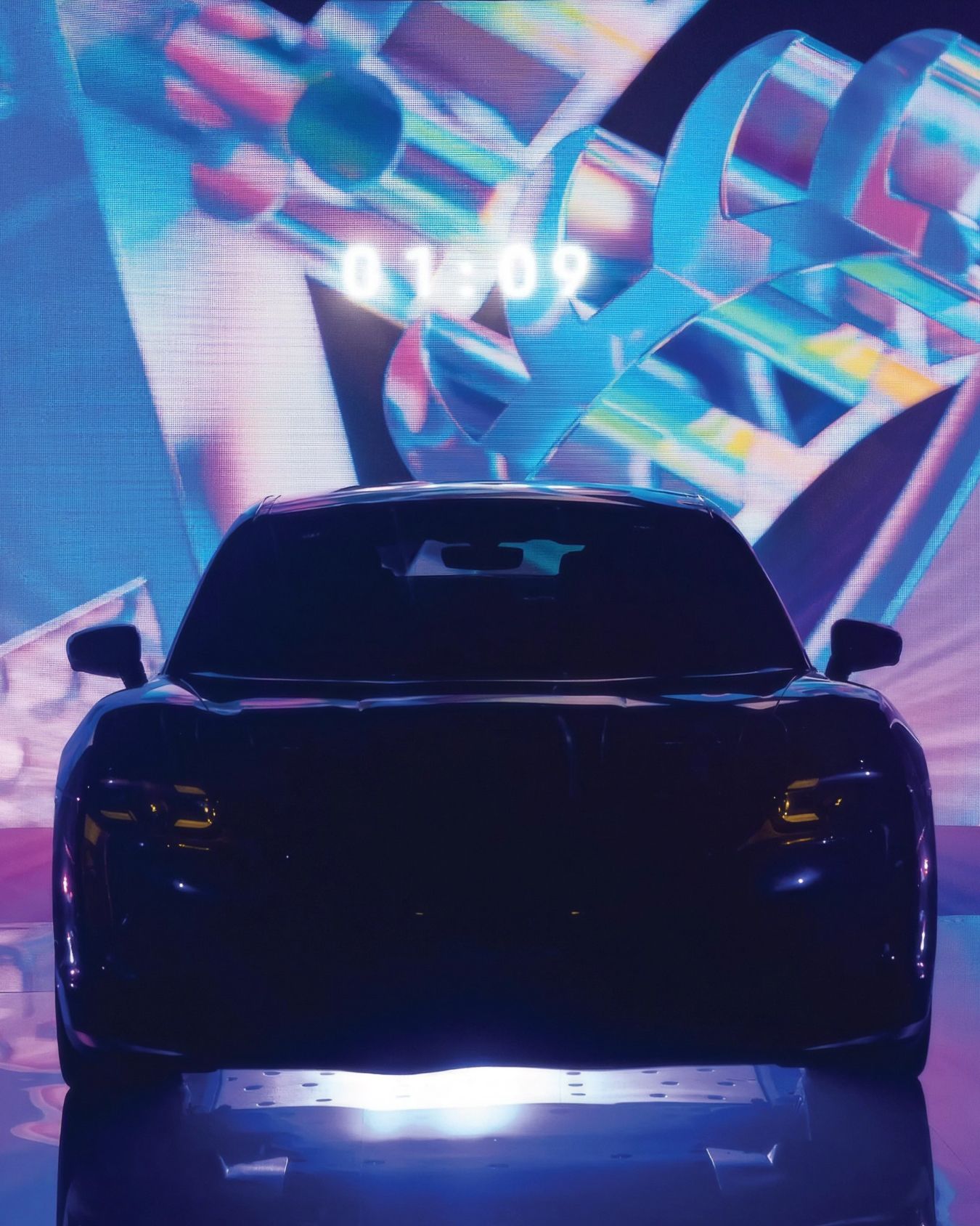 A vehicle in-front of a screen, showing a close up of the logo graphic.  