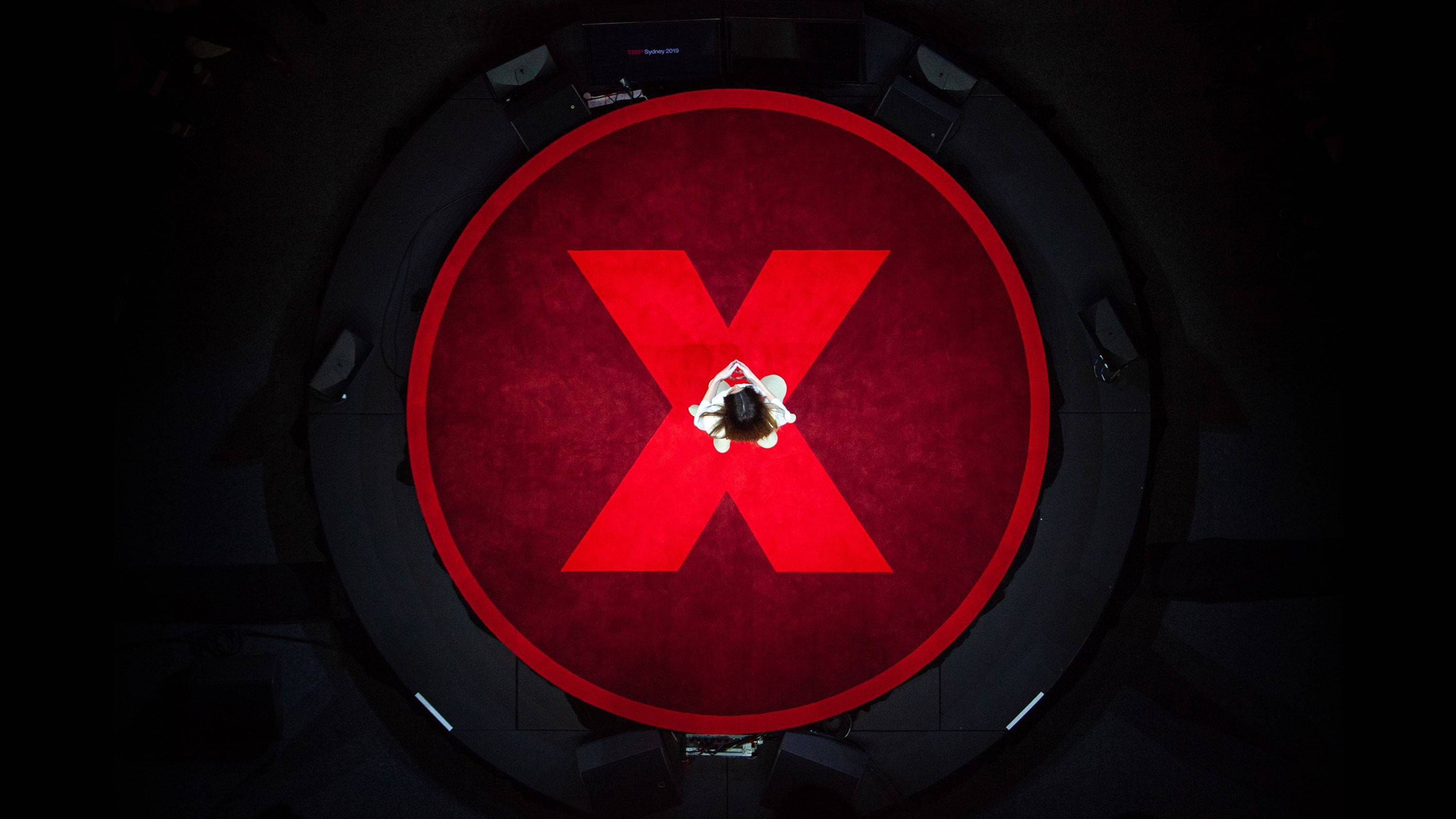 Topdown view of a person standing in the centre of a circular stage with an illuminated red logomark.