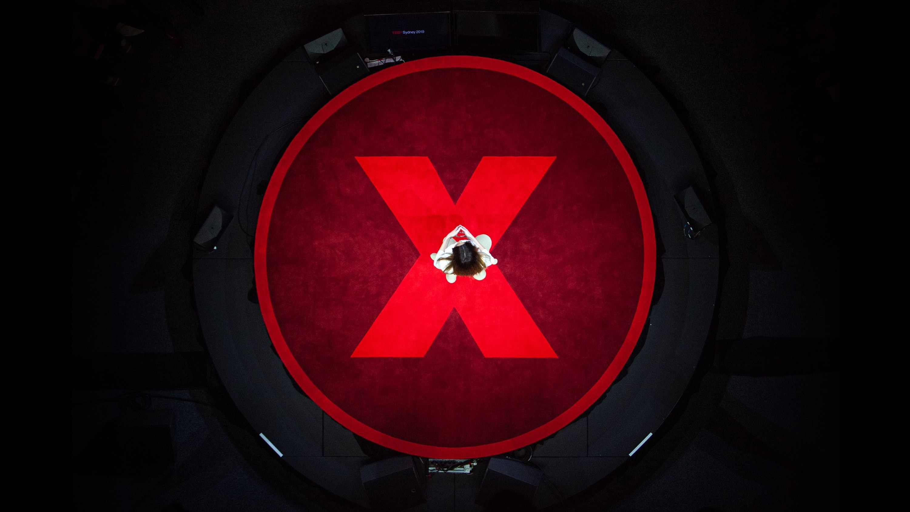 Topdown view of a person standing in the centre of a circular stage with an illuminated red logomark.