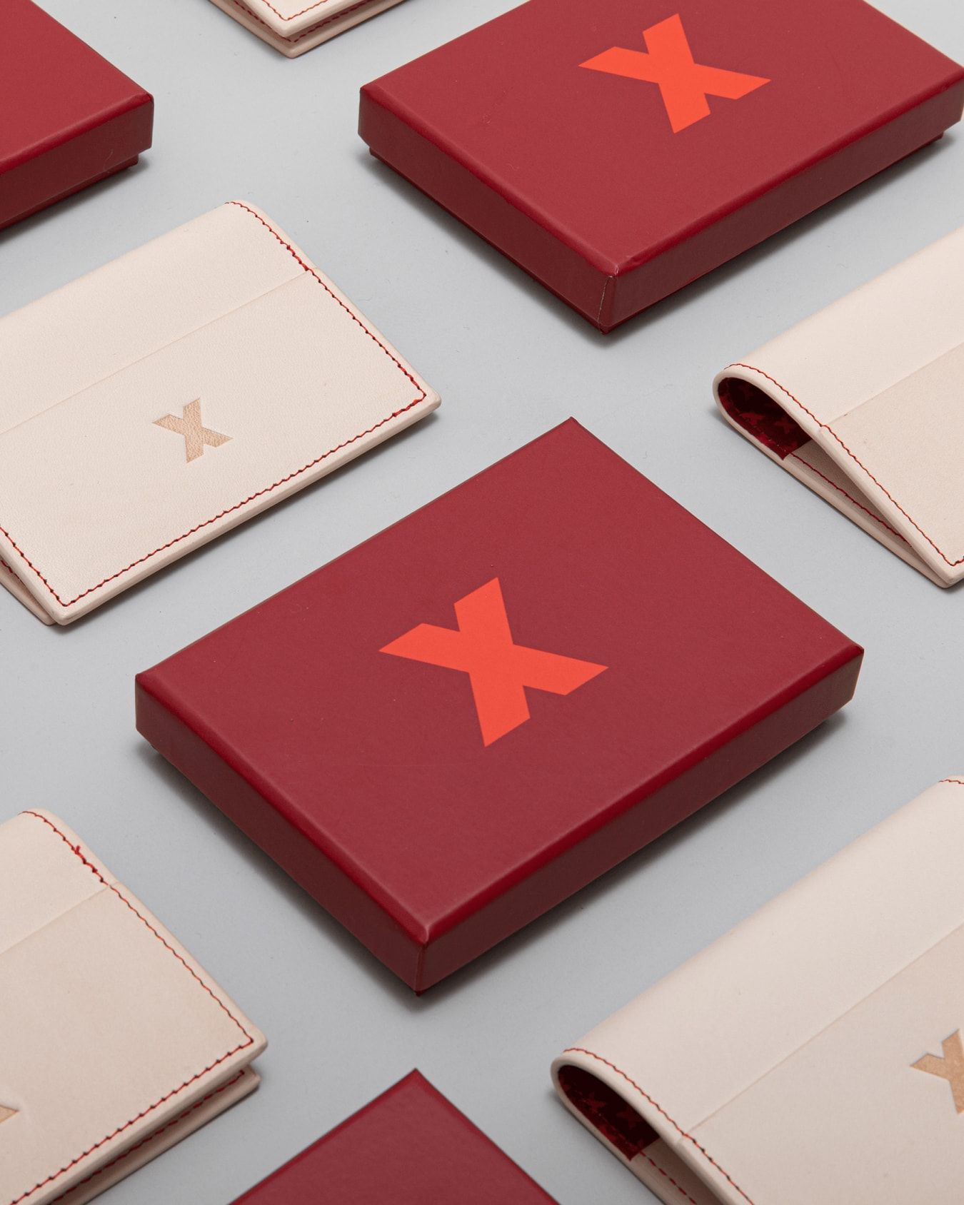 A close up crop of a cream wallet with a debossed logomark and a dark red box with a printed red logomark.