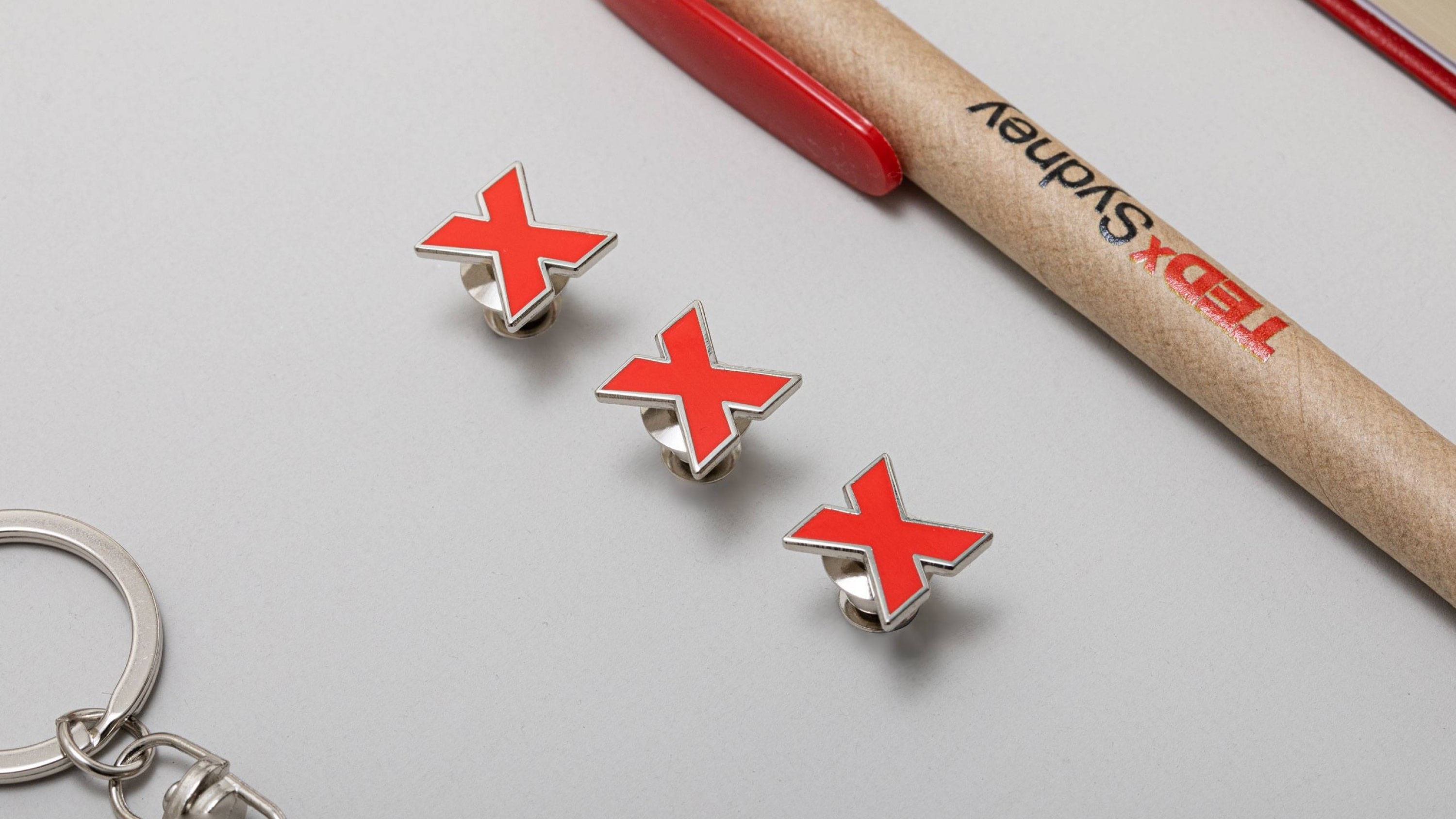 Close up of a metal badge with a red logomark and a pen with the logo.