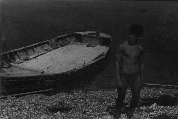 Male figure standing beside rowing boat [P46]