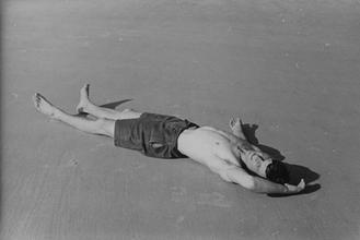 Male figure in bathing shorts lying on beach [P58]