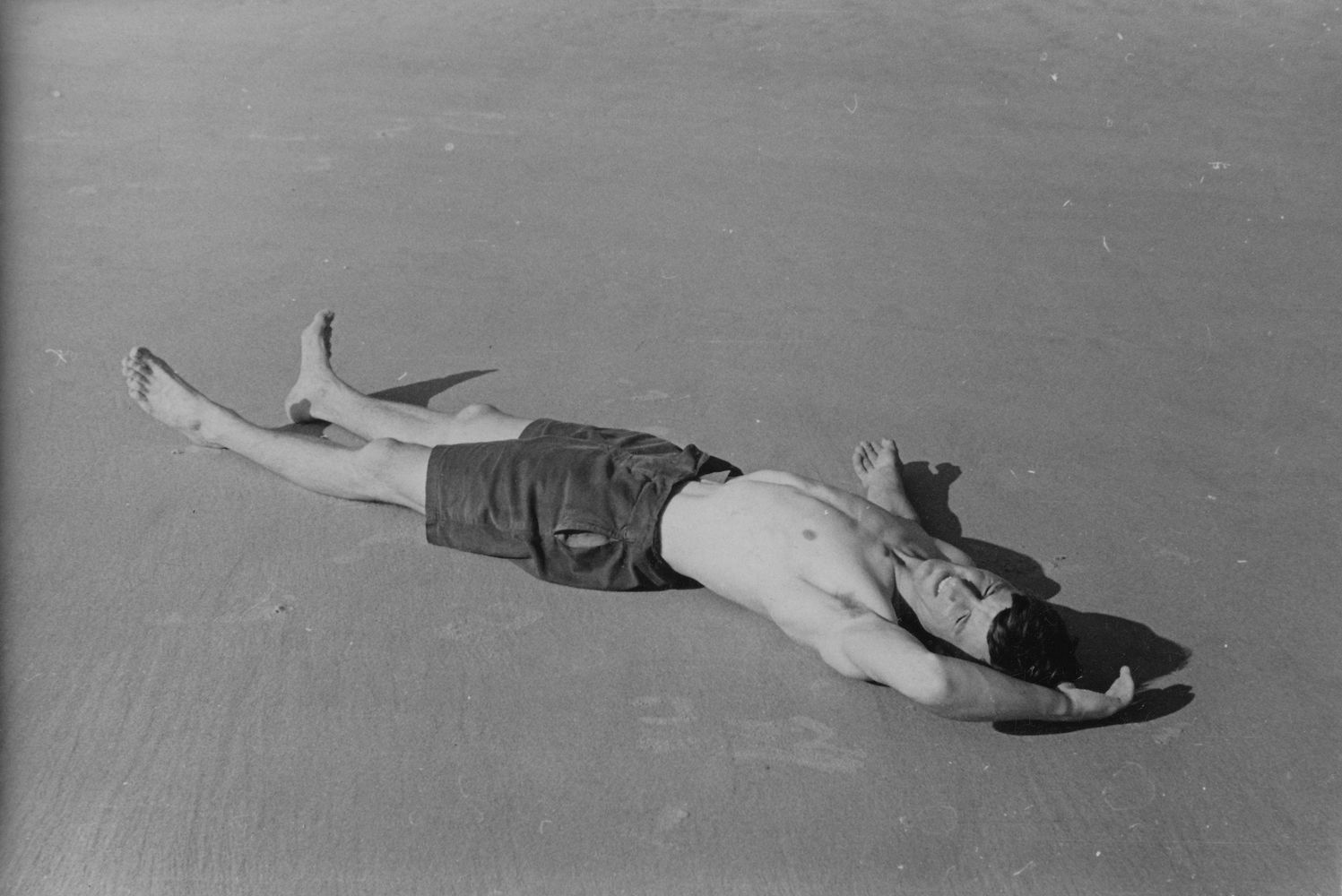 Male figure in bathing shorts lying on beach [P58]