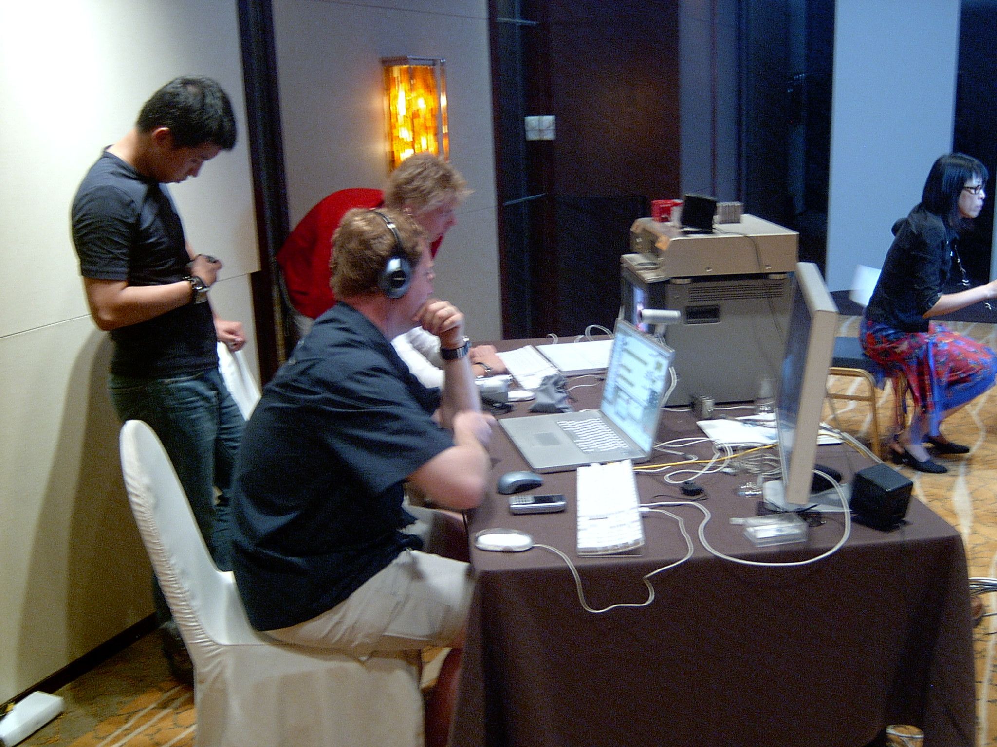 Technician in headphones at a laptop and monitor on the streaming desk, with crew around him