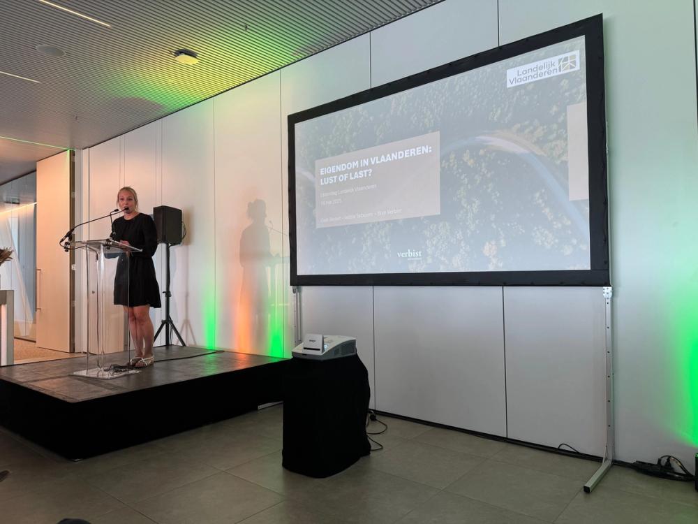 Speaker on stage at Landelijk Vlaanderen, the screen showing the title Eigendom in Vlaanderen: lust of last?