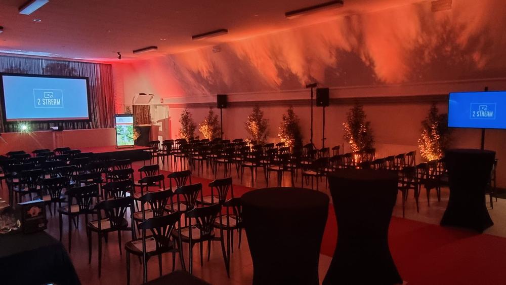 Event hall set with rows of chairs, red and orange lighting and screens showing the 2 Stream logo