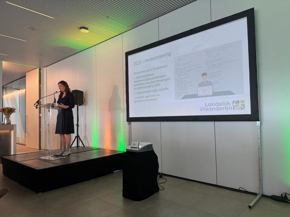 Speaker at a lectern beside a Landelijk Vlaanderen slide on the 2025 modernisation of its member database
