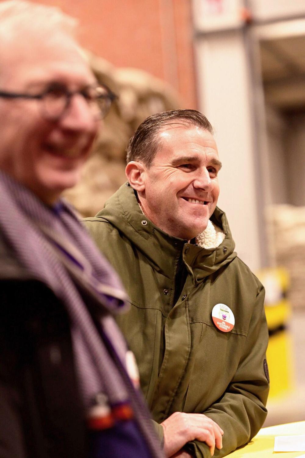 Smiling man in a green parka with a Sustainable Stories badge at the warehouse event