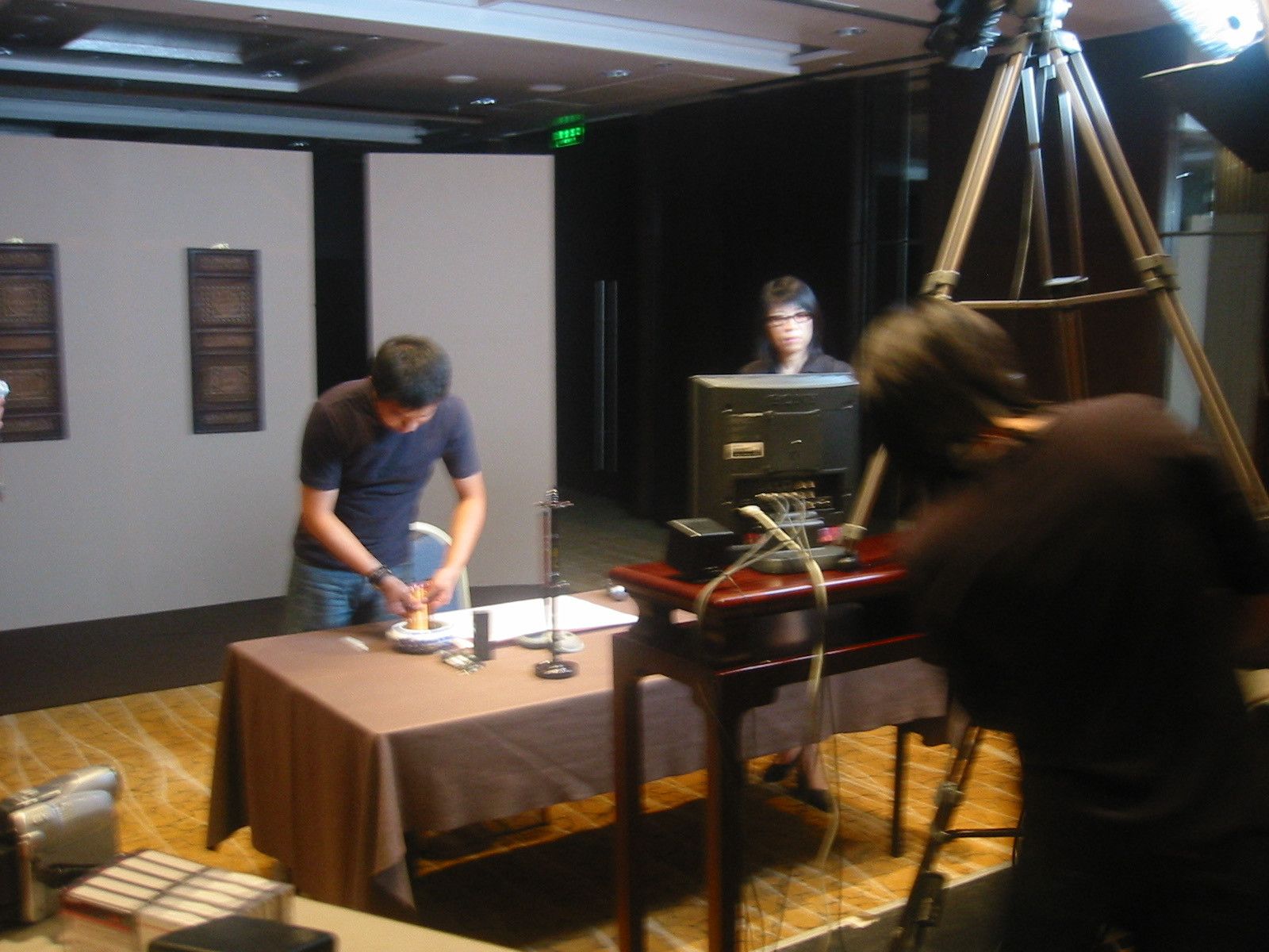 Crew member preparing a calligraphy table in front of a tripod camera and a monitor on a side table
