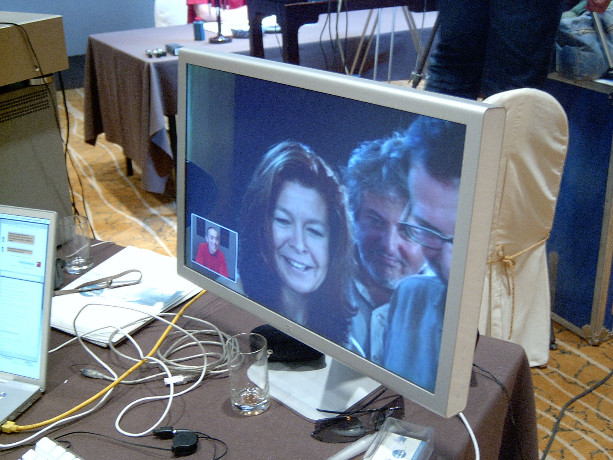 Monitor showing a video call with three smiling people, a man in red in the self-view window