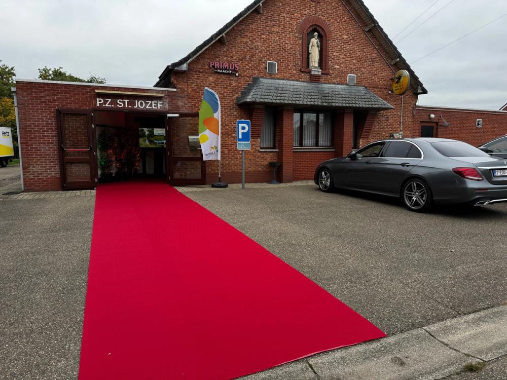 Red carpet leading to the entrance of the P.Z. St. Jozef hall, a brick building with a saint statue above