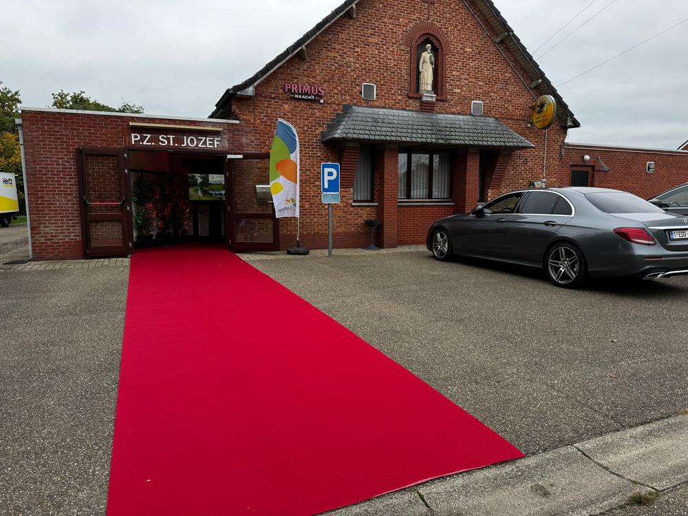 Red carpet leading to the entrance of the P.Z. St. Jozef hall, a brick building with a saint statue above