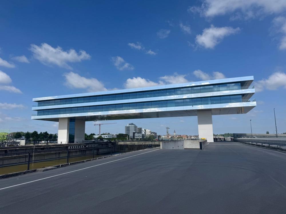 Long glass office building raised on two pillars above a dockside road under a blue sky
