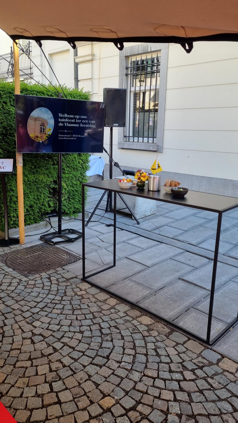 Screen welcoming guests to the De Warande garden party for the Flemish holiday, beside a high table and speaker