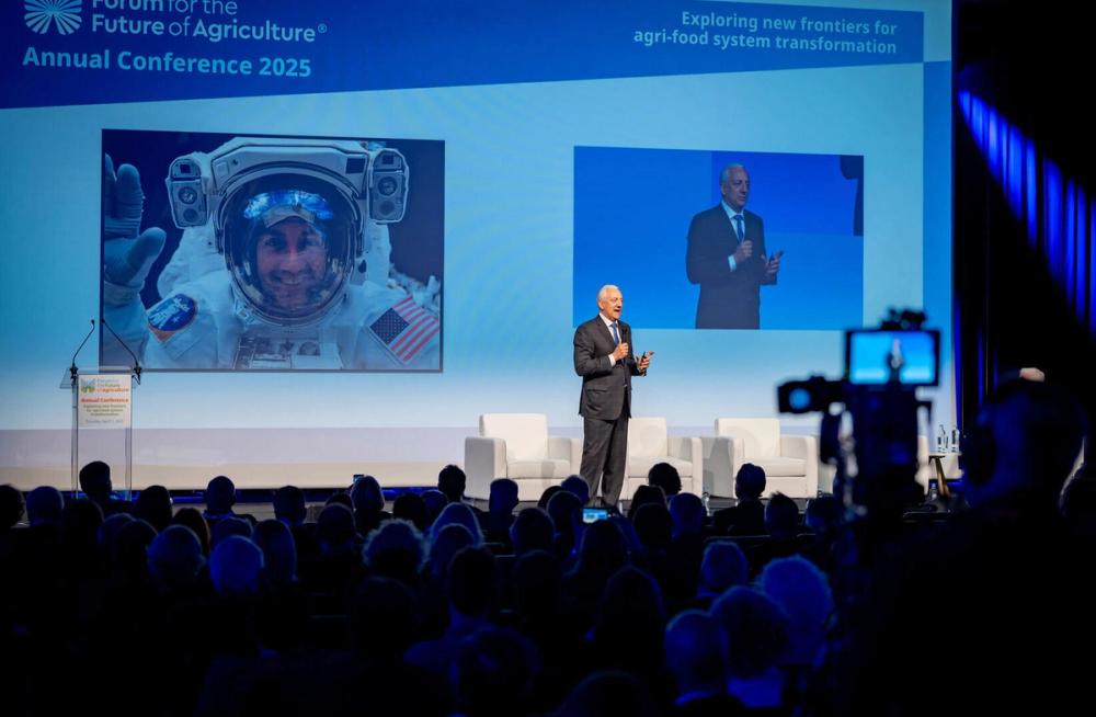 Speaker on stage at the Forum for the Future of Agriculture 2025, an astronaut on screen and a camera in front