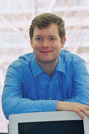 Christophe Lenaerts in a blue shirt, smiling and leaning on a computer monitor