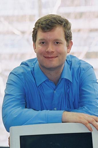 Christophe Lenaerts in a blue shirt, smiling and leaning on a computer monitor