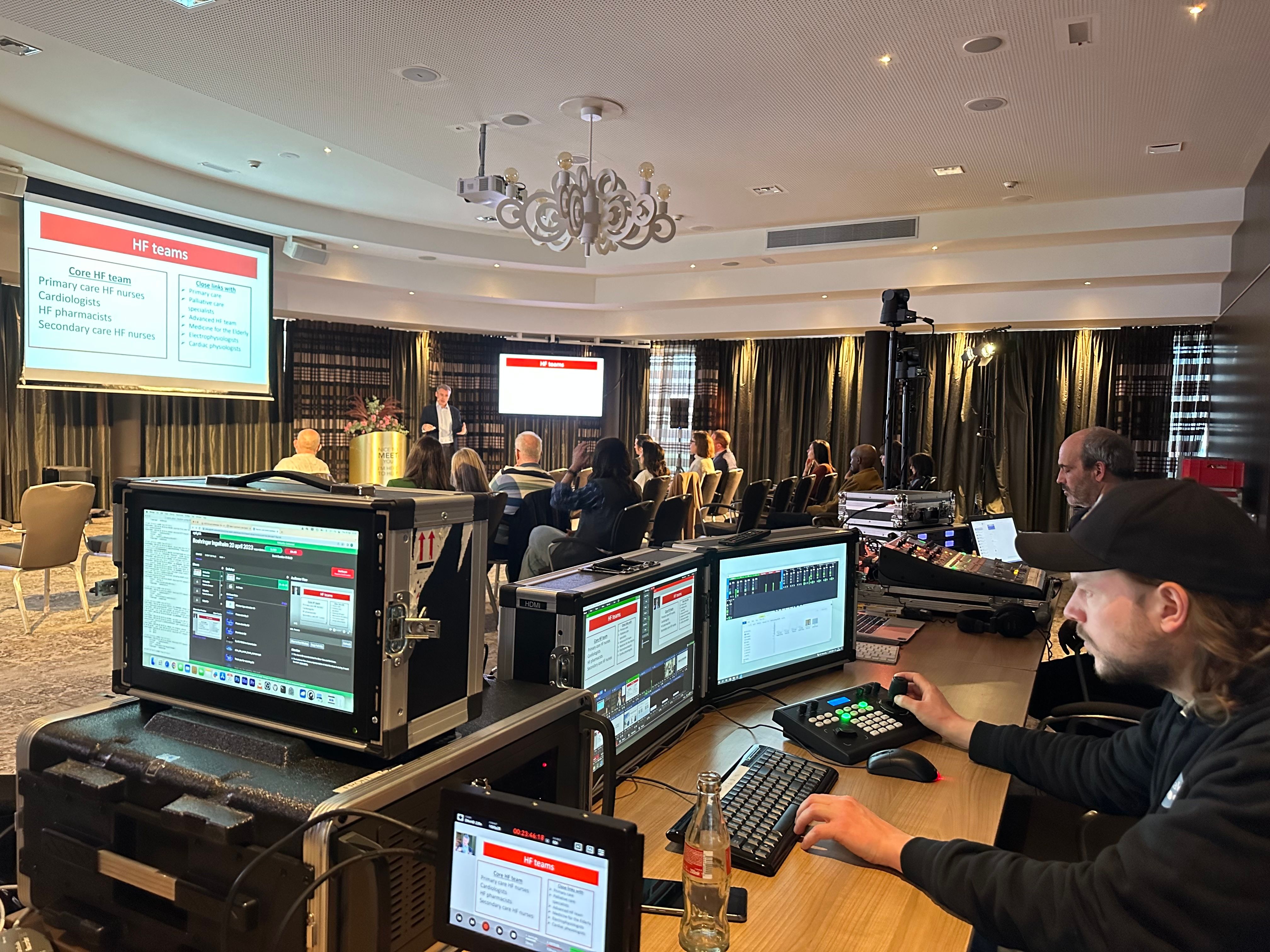 A live production desk with vision mixer and multiviewer screens at the back of an event room