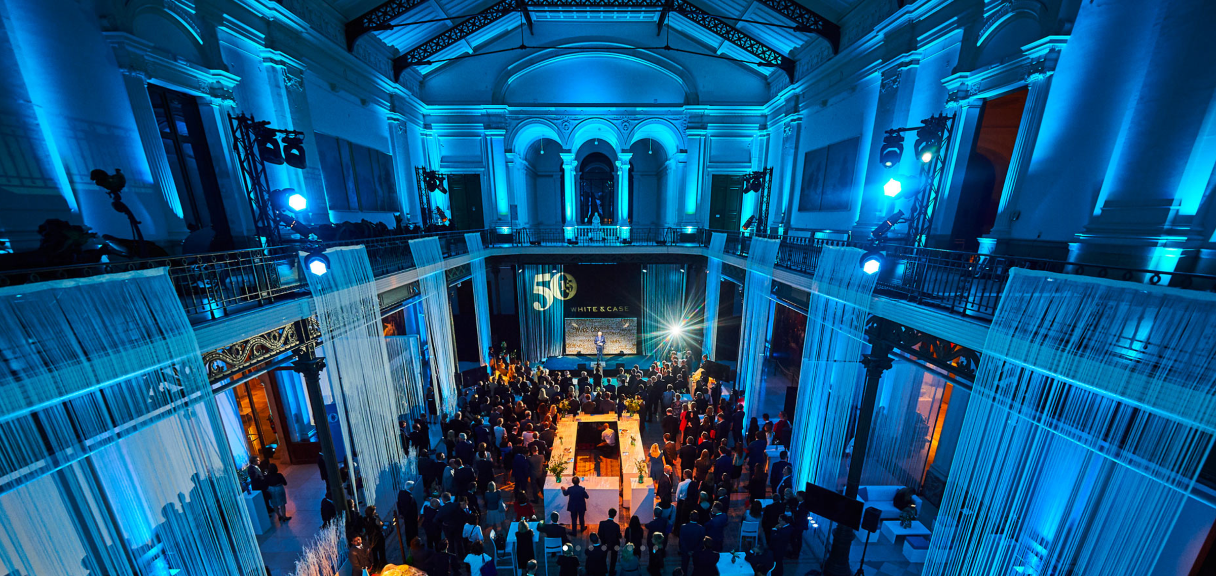 A corporate evening event in a historic hall, lit blue, with a full audience around a central stage