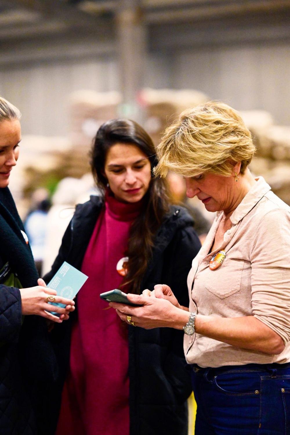 Three women looking at a phone and a small card at the event in a warehouse
