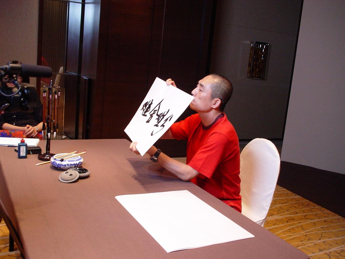Man in a red shirt holding up a sheet of Chinese calligraphy to the camera