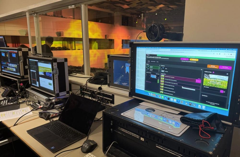 Streaming control booth with a ForumForAG 2025 EN broadcast dashboard on screen, overlooking the auditorium