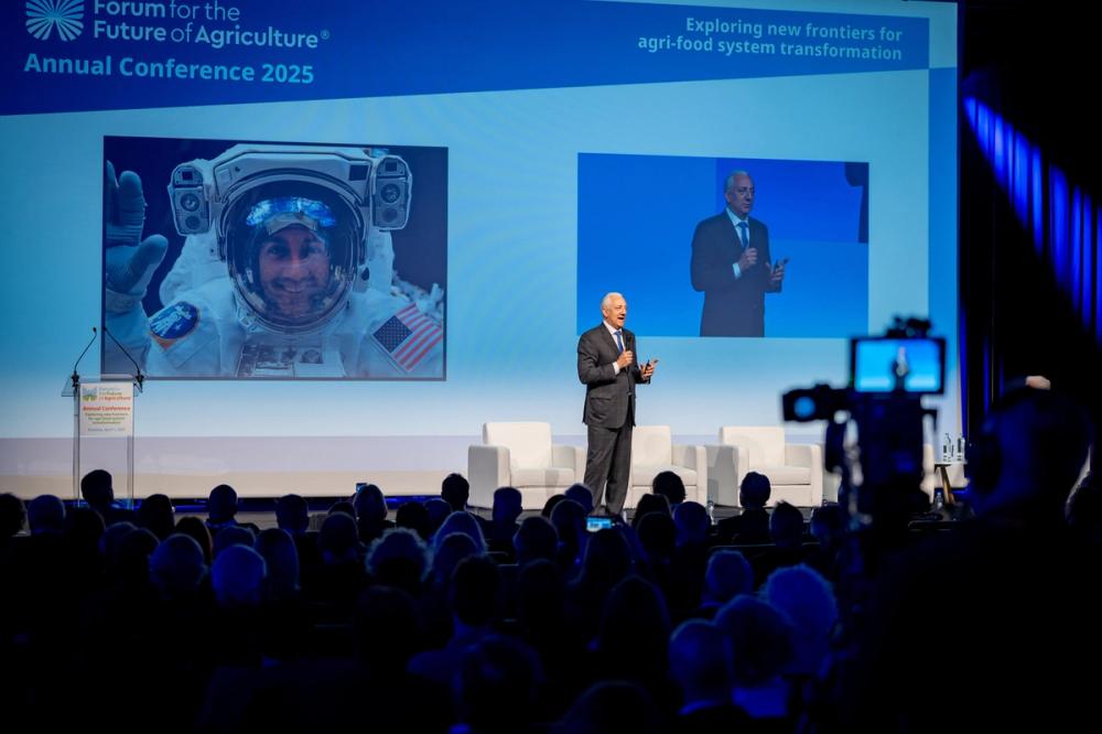 Mike Massimino speaking at the Forum for the Future of Agriculture 2025, his astronaut photo on screen and a camera in front
