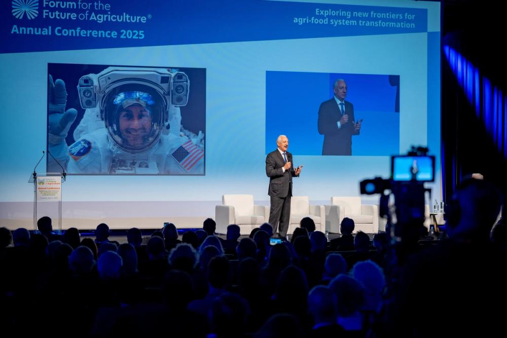 Mike Massimino speaking at the Forum for the Future of Agriculture 2025, his astronaut photo on screen and a camera in front