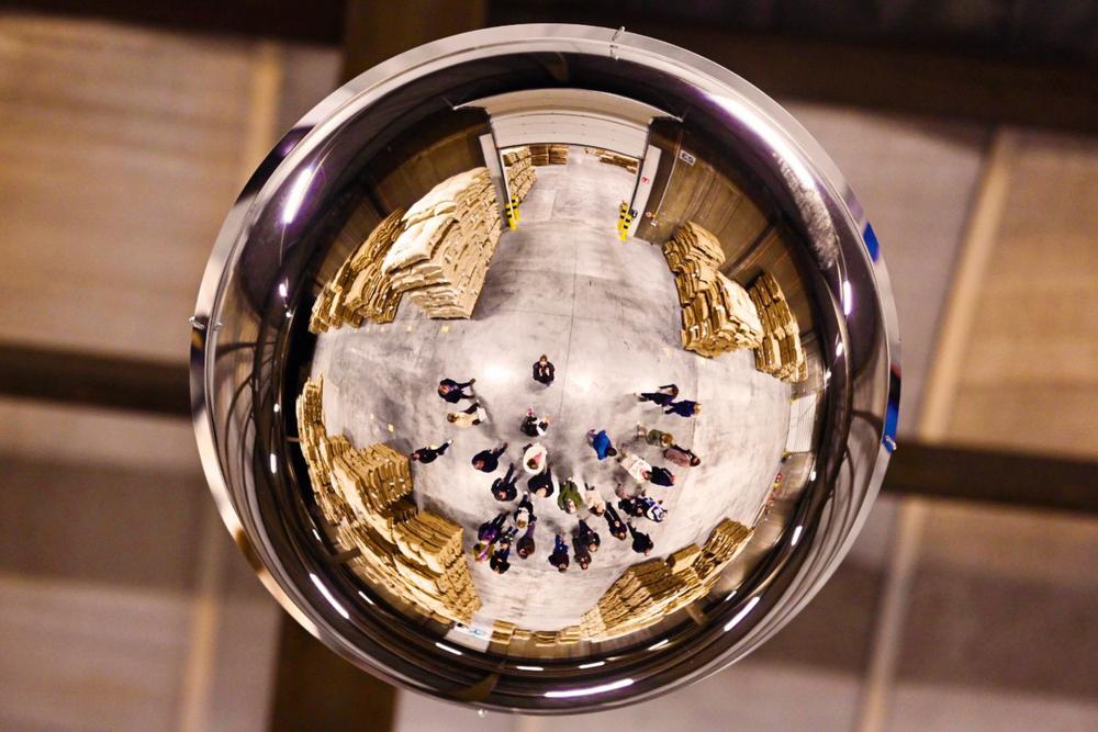 Guests in a warehouse seen from above, reflected in a round convex safety mirror