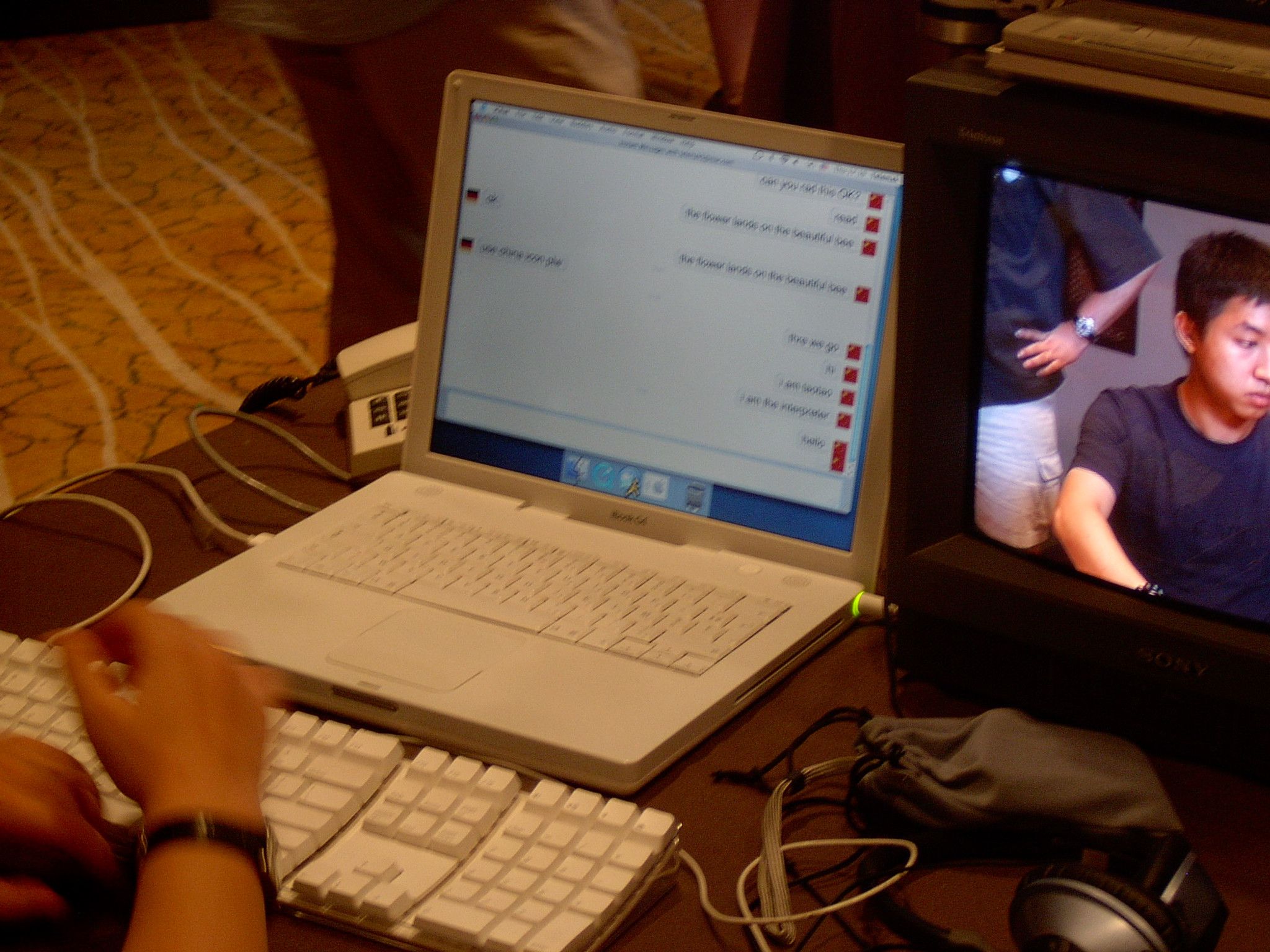 Laptop showing a chat transcript next to a Sony monitor with a live camera feed of a young man at a table