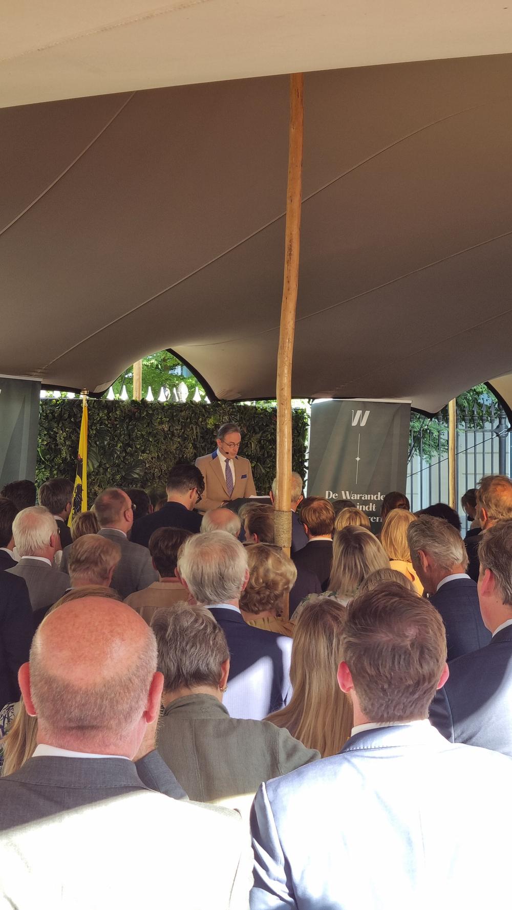 Crowd under a stretch tent listening to a speaker at a De Warande reception
