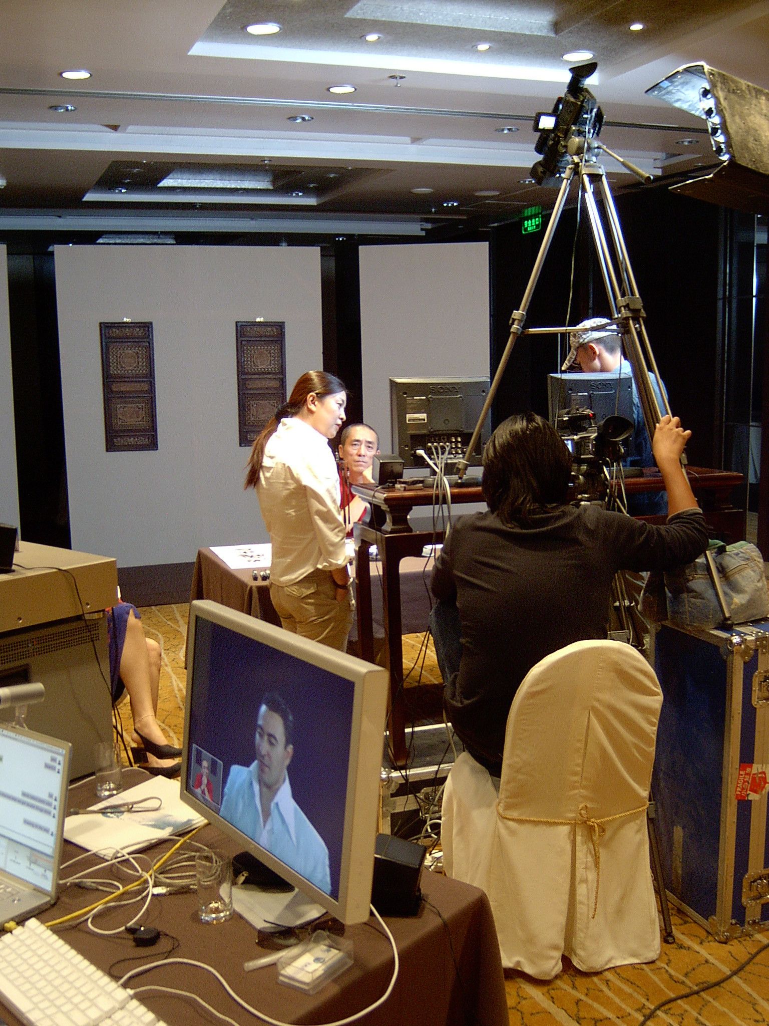 Camera operator and crew on a hotel set, a monitor in front showing a remote video call participant