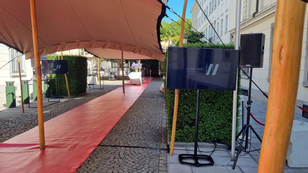 De Warande garden party entrance with a red carpet under a tent, screens with the De Warande logo and speakers