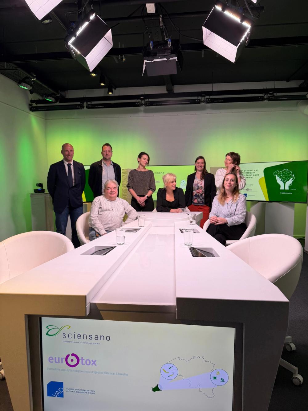 Eight people posing at a white studio desk whose screen shows the Sciensano, Eurotox and VAD logos