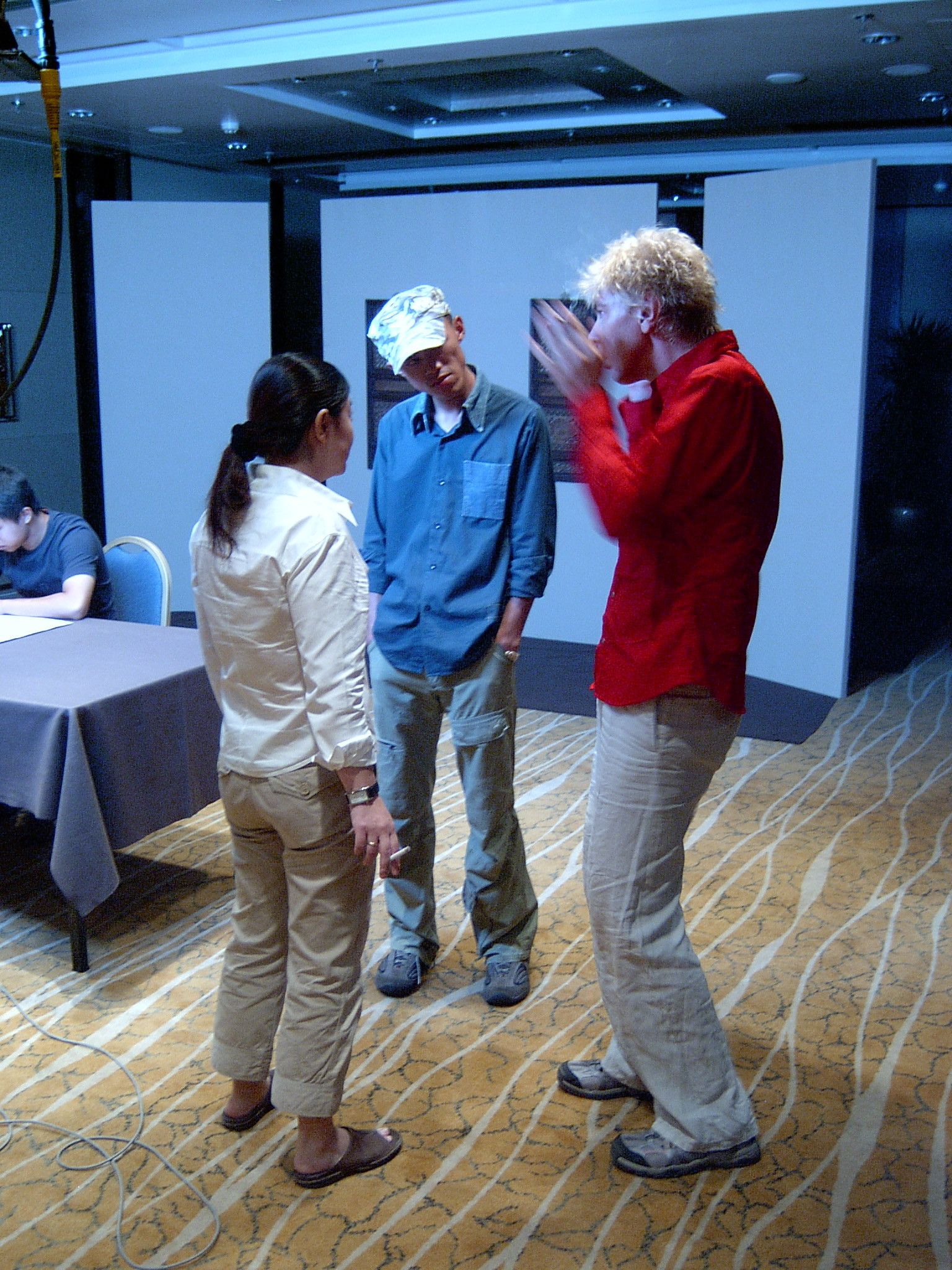 Three crew members talking on a patterned carpet between white partition walls in a hotel function room