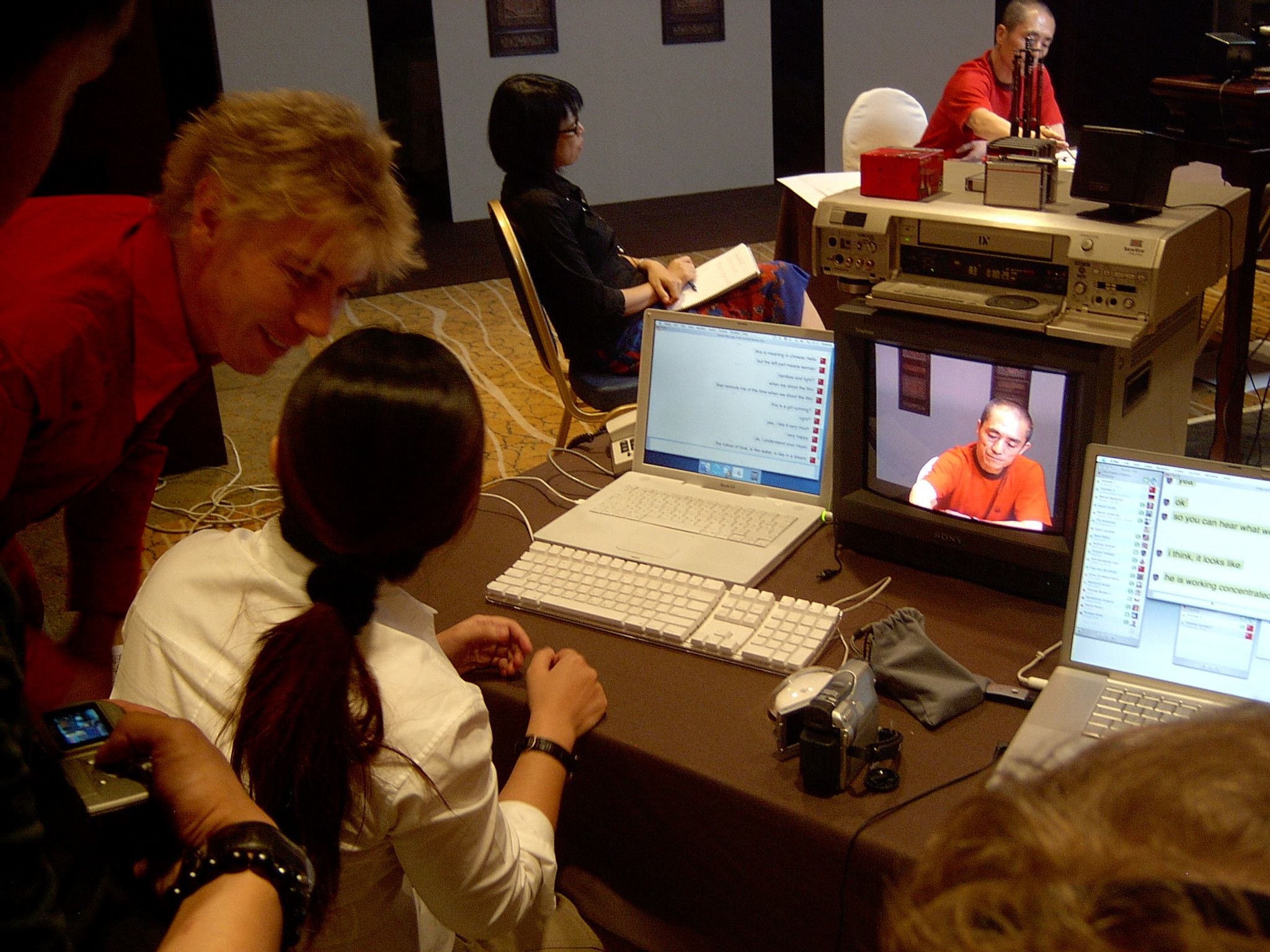 Operator at a laptop showing a live chat while a CRT monitor shows a man in orange on camera