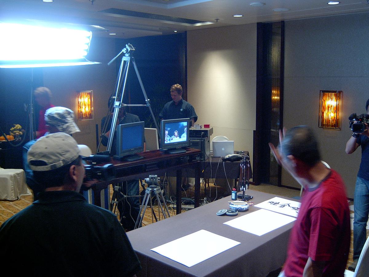 Hotel function room set up for the stream: lights, tripods, monitors and a table laid with paper for calligraphy