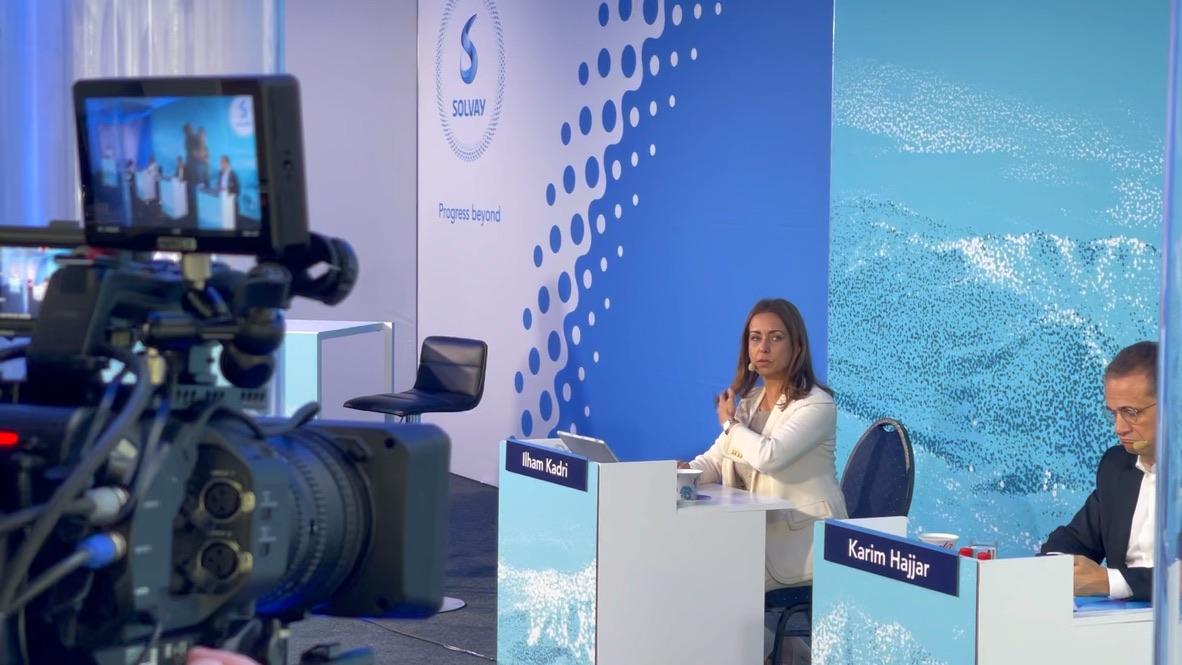 A broadcast camera trained on a speaker at a branded corporate set during a live stream