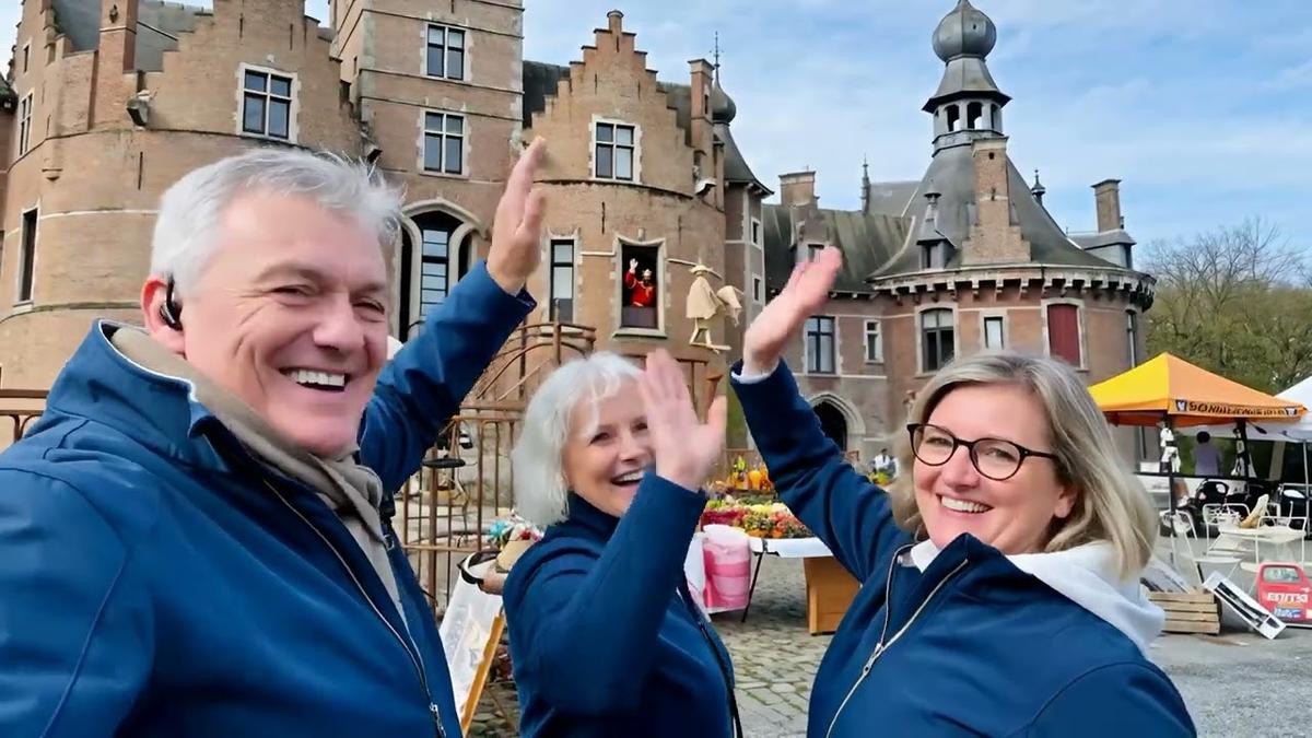 Three people in matching blue jackets waving in front of Ooidonk Castle at the Lifestyle Tuinbeurs