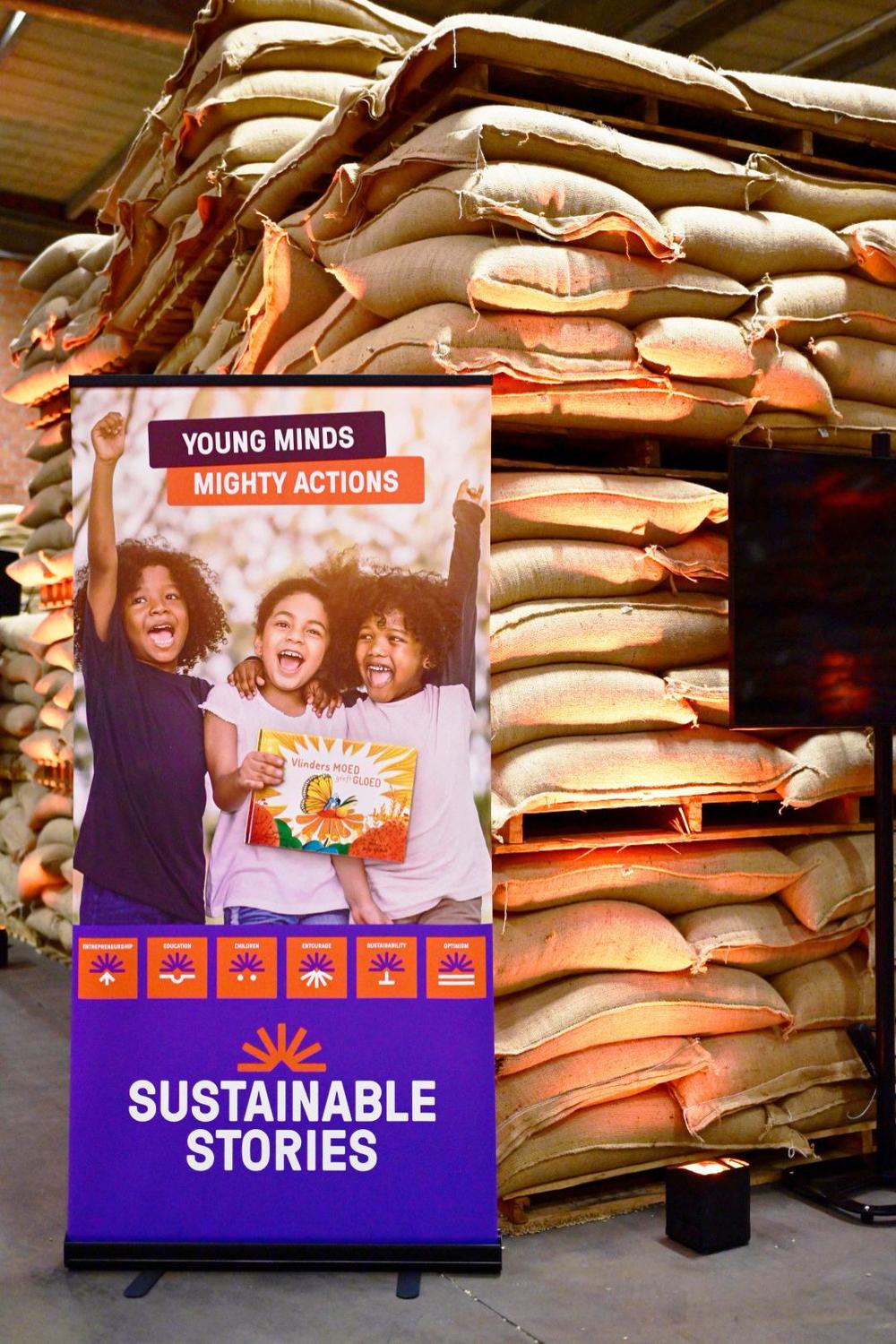 Sustainable Stories banner reading Young Minds Mighty Actions, in front of stacked burlap sacks in a warehouse