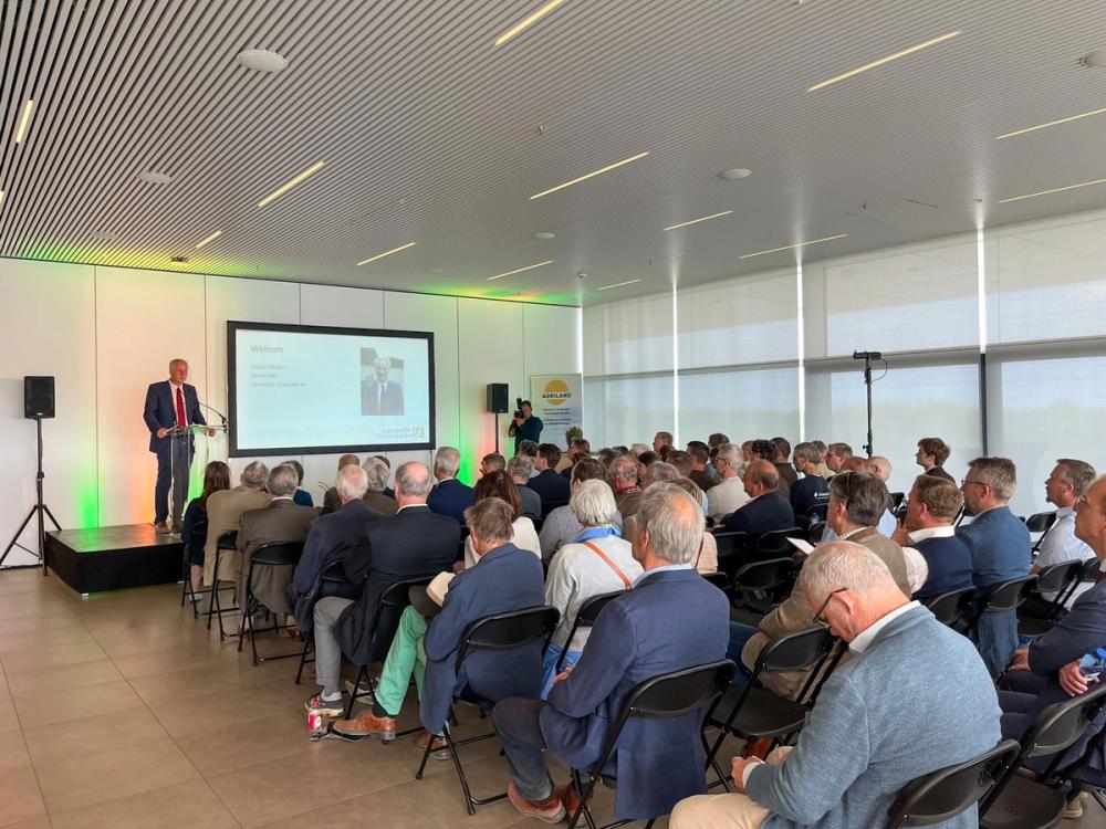 Speaker at a lectern addressing a full seated audience at a Landelijk Vlaanderen event, a welcome slide on screen