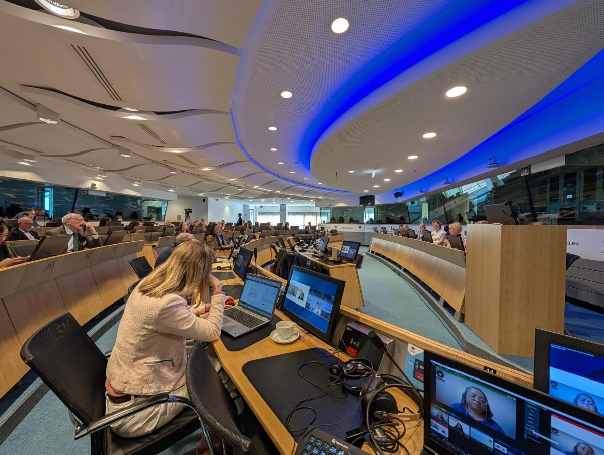 Hybrid FAO meeting in a curved conference room, delegates at laptops and remote speakers shown on desk monitors