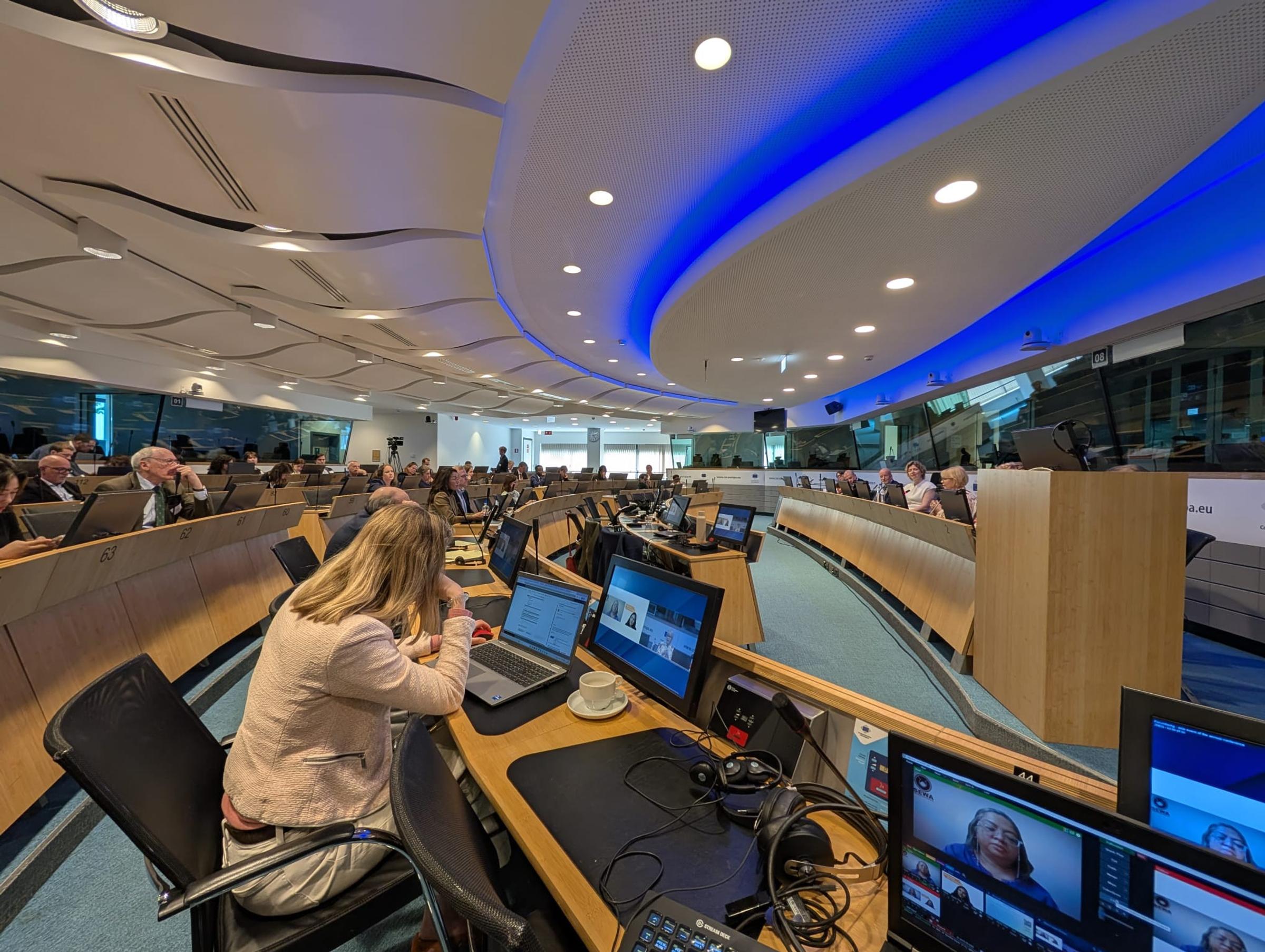 Hybrid FAO meeting in a curved conference room, delegates at laptops and remote speakers shown on desk monitors