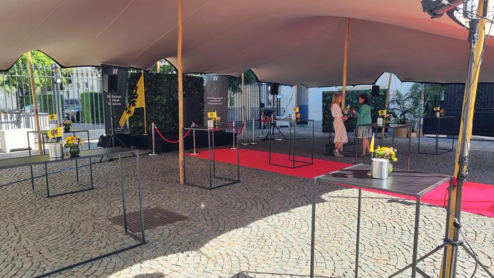 Tented courtyard at De Warande with standing tables, a red carpet, Flemish lion flags and speakers on stands