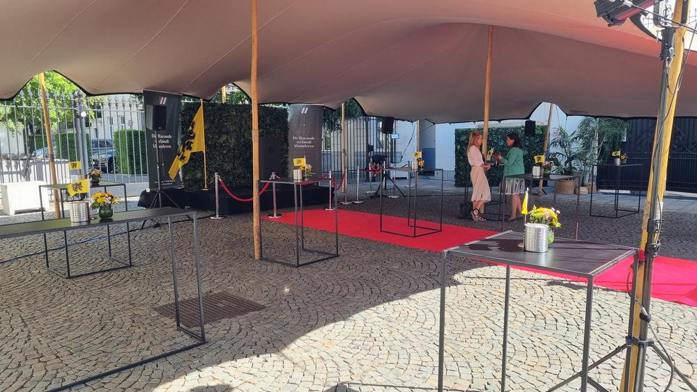 Tented courtyard at De Warande with standing tables, a red carpet, Flemish lion flags and speakers on stands