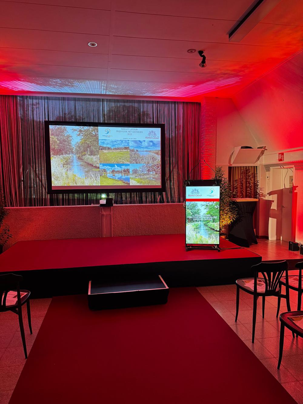 Stage lit in red for the Baillet Latour environment prize, with a projection screen and a lectern screen