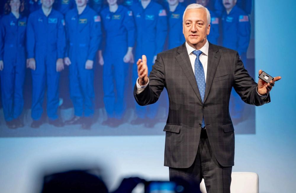 Speaker on stage at the Forum for the Future of Agriculture, in front of a photo of astronauts in blue suits