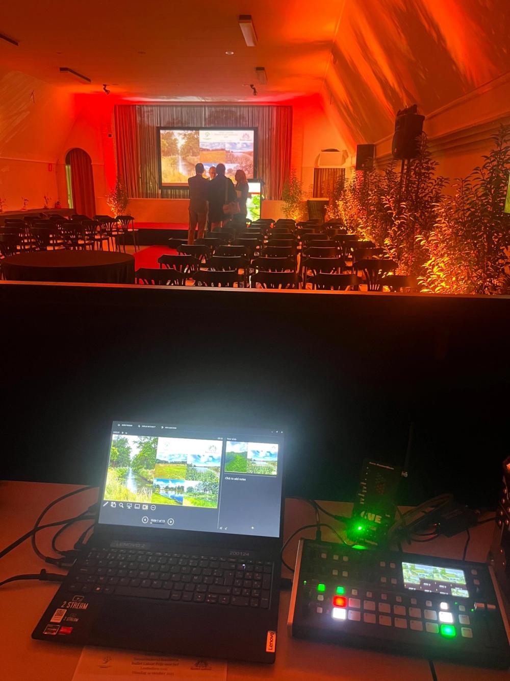 Laptop and video switcher on the tech desk, overlooking a red-lit hall set up for the Baillet Latour award