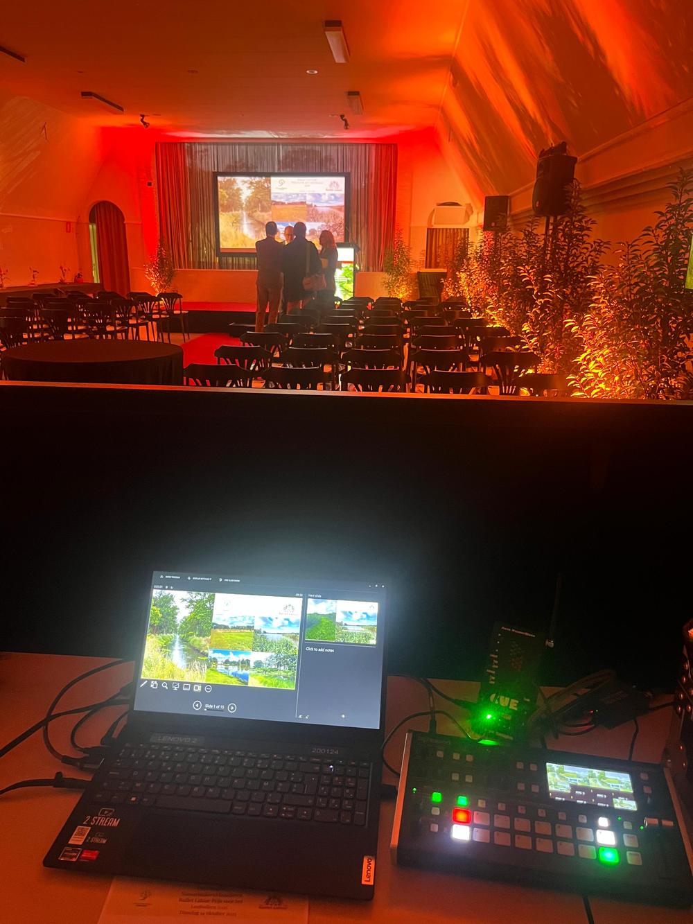 Laptop and video switcher on the tech desk, overlooking a red-lit hall set up for the Baillet Latour award